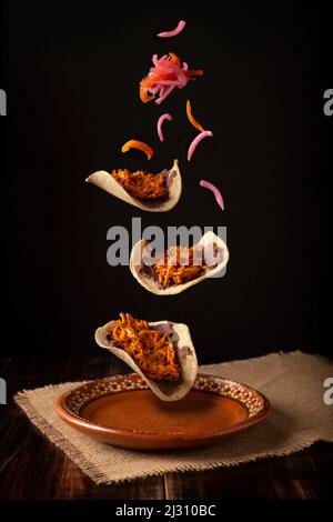Creative food image of Mexican Tacos de Cochinita Pibil and onion with habanero chili falling on traditional mexican clay dish. Levitation photography Stock Photo