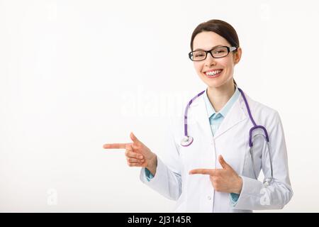 Portrait of confident young medical doctor on white background. Doctor points to to copy space Stock Photo