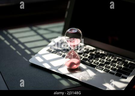 Hourglass sand timer on top of laptop. Passing time, countdown or deadline concept. Stock Photo