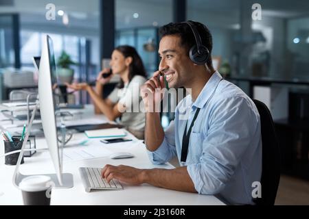 Dedicated service creates dedicated customers. Shot of a young man using a headset and computer in a modern office. Stock Photo
