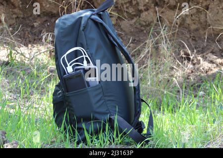 Smartphone charged with black power bank in green backpack. Close up. Stock Photo