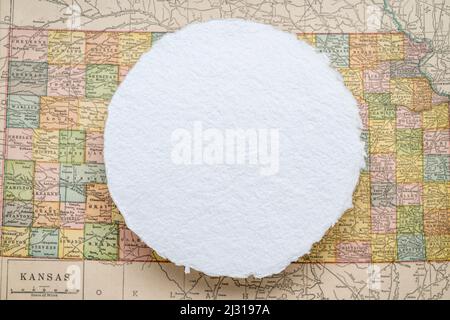 blank, circular sheet of rough handmade paper floating over vintage defocused map of Kansas State Stock Photo