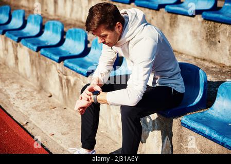 Man sitting at stadium seat and checking fitness watch after exercises Stock Photo