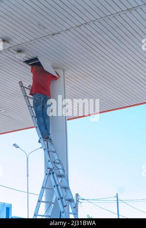 A worker on a stepladder checks or repairs something in a hatch on the ceiling Stock Photo