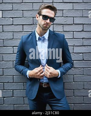 Hes got the look. Shot of a handsome young businessman standing against a grey facebrick wall. Stock Photo