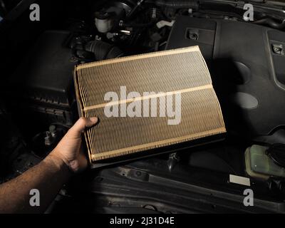 A mechanic holds a car air filter in his hand for auto maintenance in a repair shop, automotive part concept Stock Photo