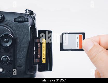 Photographer hand insert memory SD card to memory slot of the digital DSLR camera,isolated on white background Stock Photo
