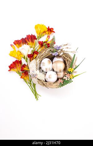 Bouquet of yellow and red flowers with nest with colored eggs on white background. Happy Easter. Vertical. Copy space Stock Photo
