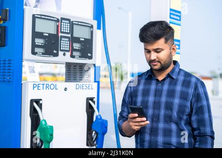 customer at petrol pump using mobile phone - concept of using social media, technology and communication. Stock Photo