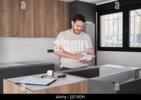 Young hispanic man read instruction manual before installing kitchen furniture. Stock Photo