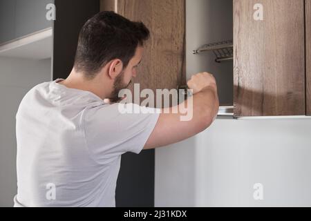 Young latin man installing cupboard in the kitchen using a screwdriver. Stock Photo