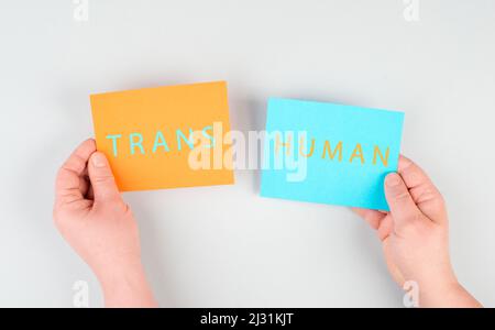 The word transhuman is standing on two pieces of paper, holding the message in the hands, future technology, post human, science, transformation Stock Photo