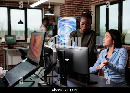 3D graphic diverse artists in office workspace conversating about design of project. Development department team leader helping coworker with software issue while working on digital art. Stock Photo