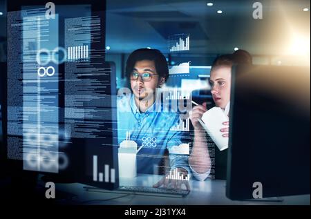 Cracking codes through the night. Shot of two focused young male programmers working together on a computer while eating noodles in the office at Stock Photo
