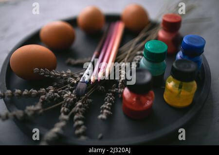 Multicolour paints and brushes on the plate with eggs. Colouring eggs for easter holiday concept. Stock Photo