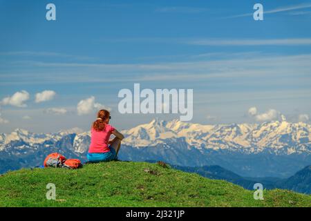 Woman while hiking sits on meadow and looks at Hohe Tauern with Grossglockner, from Rinderfeld, Dachstein, UNESCO World Heritage Hallstatt, Salzburg, Austria Stock Photo