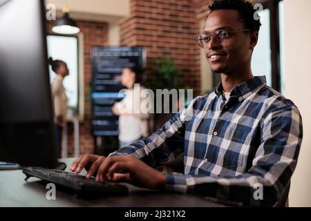 Smiling confident african american software engineer developing machine learning algorithm in order to sustain system security stability. Cyber developer creating network using binary encryption. Stock Photo