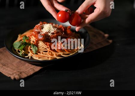 Female or chef hands putting some fresh tomato on a plate of spaghetti. Italian pasta cuisine. Spaghetti with homemade tomato sauce. Stock Photo