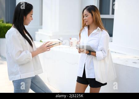 Two Asian college students were talking and discussing their final project in the outside of the campus building. A female university student intervie Stock Photo
