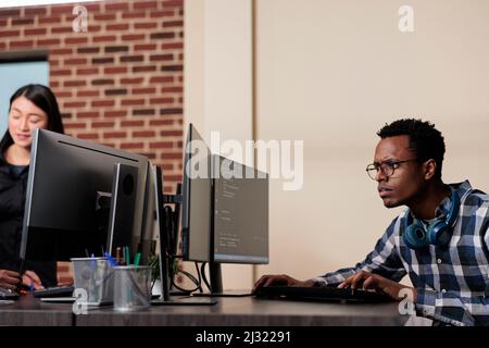 Confused tech engineer sitting doubtful at computer trying to solve network processing errors. Computer programmer puzzled by nonfunctional security algorithm and company corrupted database. Stock Photo
