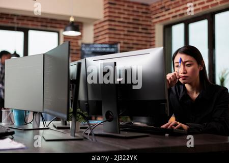 Meditative asian program engineer thinking of ways to combat hacking attacks. Thoughtful blockchain developer reflecting at low levels of security and how to improve mainframe defence system. Stock Photo