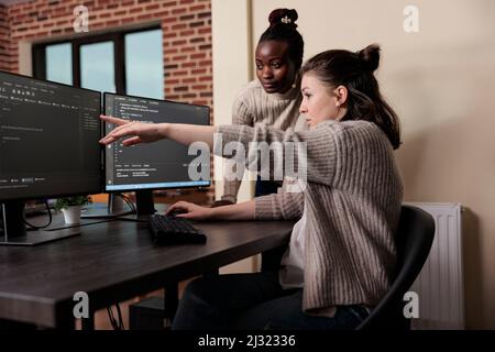 Caucasian network developer pointing out high usage of processing power in mainframe grid. African american programmer helping coworker to solve overloaded system storage space. Stock Photo