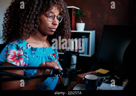 Young curly hair black woman podcasting with microphone at the computer Stock Photo