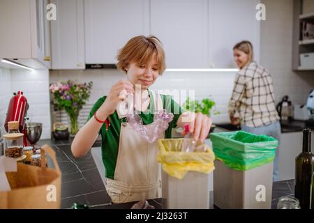 Teen girl throwing plastic bottles in recycling bin in the kitchen. Stock Photo