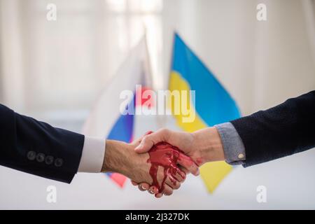 Representatives of Ukraine and Russia shaking hands, blood hand concept. Stock Photo