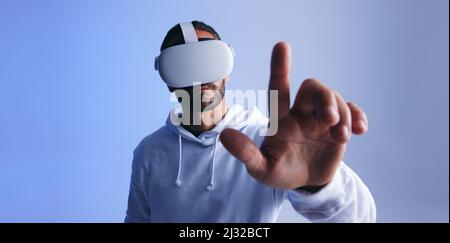 Man touching a button in virtual space. Young man interacting with the metaverse using a virtual reality headset. Young man experiencing a 3D simulati Stock Photo