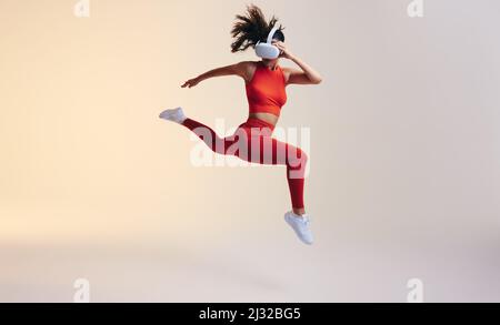 Young woman working out with 3D technology. Athletic young woman jumping mid air while wearing a virtual reality headset. Sporty young woman exploring Stock Photo