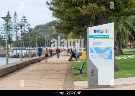 People exercising, walking and riding bicycles along the foreshore footpath near Queens Wharf, Newcastle Harbour towards Nobbys Head in Australia Stock Photo