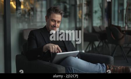 Businessman using tablet computer in office. Happy middle aged man in business casual, Entrepreneur working online, reading finance report, thinking. Stock Photo
