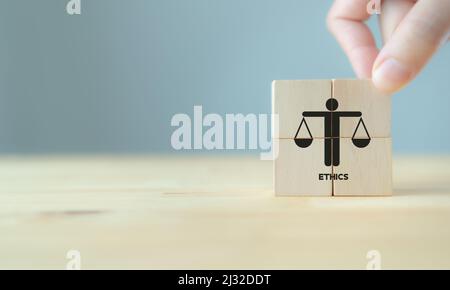 Business ethics concept. Business moral principles concept.  Hand holds the wooden cubes with 'ETHICS' symbols on grey background and copy space. Bann Stock Photo