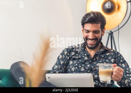 Handsome Latin American Enterpreneur Sitting on Sofa and Working on his laptop in living room while sipping on Latte Coffee. High quality photo Stock Photo