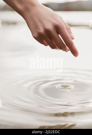 A hand reaches into the water and drips, an image of contemplation, mindfulness, and embodiment Stock Photo