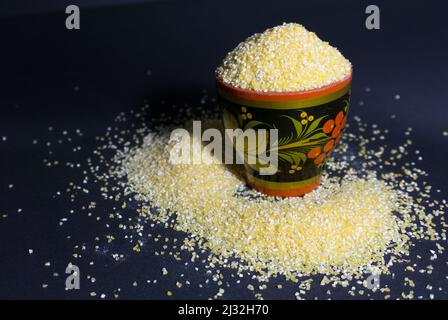 Raw corn grits flour in a wooden bowl on black background Stock Photo
