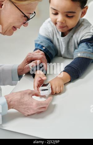 Mature pediatrician measuring level of oxygen in blood with pulse oximeter on finger of cute little patient in medical office Stock Photo