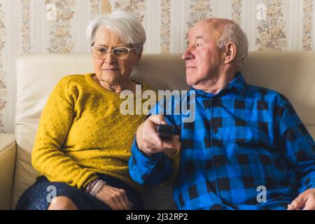 Portrait of an elderly couple watching television while sitting on the sofa - man is holding the remote control. High quality photo Stock Photo