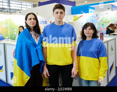 Berlin, Germany. 05th Apr, 2022. Natalia Netudykhata (l-r), her 17-year-old son Kyrylo and Tatiana Nikolaeva stand at the Fruit Logitica fair with Ukrainian flags and sweaters. They are employees of the Artberry company and their plantation is in Ukraine. They represent their husbands at the fair, who do not leave their country because of the war. Natalia, Kyrylo and Tatiana return to Kiev after the fair. Credit: Annette Riedl/dpa/Alamy Live News Stock Photo