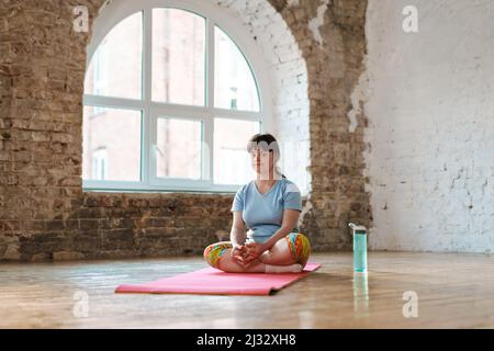 Young woman with down syndrome sitting on fitness mat indoors Stock Photo