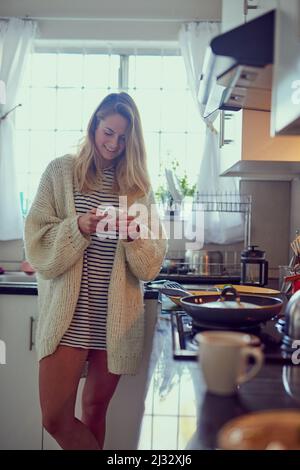 Lunch is ready, where are you. Cropped shot of an attractive young woman texting on a cellphone while cooking in her kitchen. Stock Photo