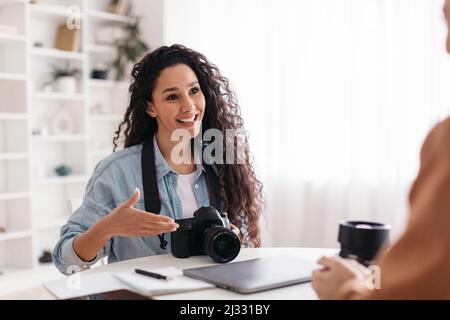 Positive Photographer Woman Talking To Lady Sitting In Modern Office Stock Photo