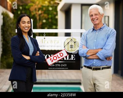 Cropped portrait of an attractive young real estate agent and her male client standing with their arms crossed next to a sold sign outside of his Stock Photo