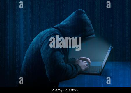 Hacker. Hacker using laptop on dark binary code digital background. Dangerous Hooded Hacker attack. Breaks into Data Servers. Hacking and malware conc Stock Photo