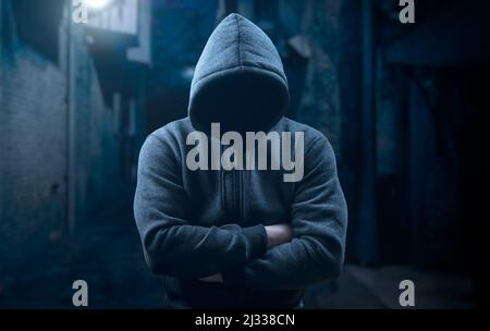 dangerous criminal. scary hooded man at night in dark alley. silhouette bandit, criminal with an unrecognizable face in threatening pose at night on d Stock Photo