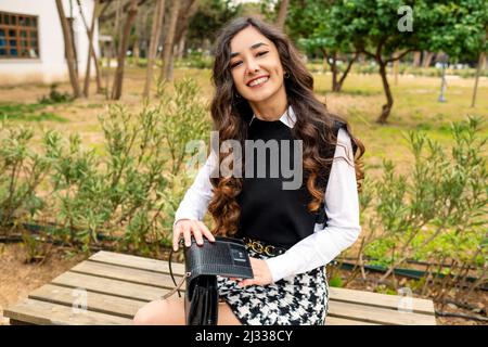Handbag, young woman holding handbag and smiling, businesswoman sitting on park bench Stock Photo