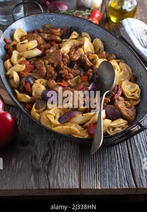 Tortellini dish with sauteed meat, vegetables and sauce in a rustic roasting pan. Italian cuisine Stock Photo