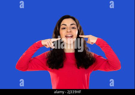 Strong healthy straight white teeth. Close up portrait of happy brunette girl wearing red t-shirt on a over blue background with beaming smile pointin Stock Photo