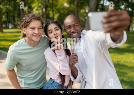 Student's selfie. Happy diverse university friends taking self-portrait on smartphone outdoors and sincerely smiling Stock Photo
